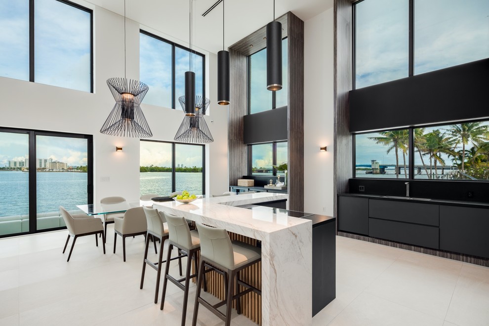 Offene Moderne Küchenbar mit flächenbündigen Schrankfronten, schwarzen Schränken, Rückwand-Fenster, Kücheninsel, beigem Boden und schwarzer Arbeitsplatte in Miami