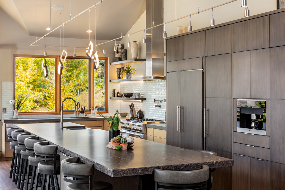 Urige Küche in L-Form mit Landhausspüle, flächenbündigen Schrankfronten, dunklen Holzschränken, Elektrogeräten mit Frontblende, dunklem Holzboden, Kücheninsel, braunem Boden und grauer Arbeitsplatte in Denver