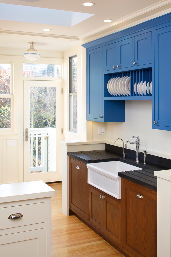 На фото: кухня в классическом стиле с с полувстраиваемой мойкой (с передним бортиком), фасадами в стиле шейкер, синими фасадами, светлым паркетным полом, деревянной столешницей, синим фартуком и цветной техникой с