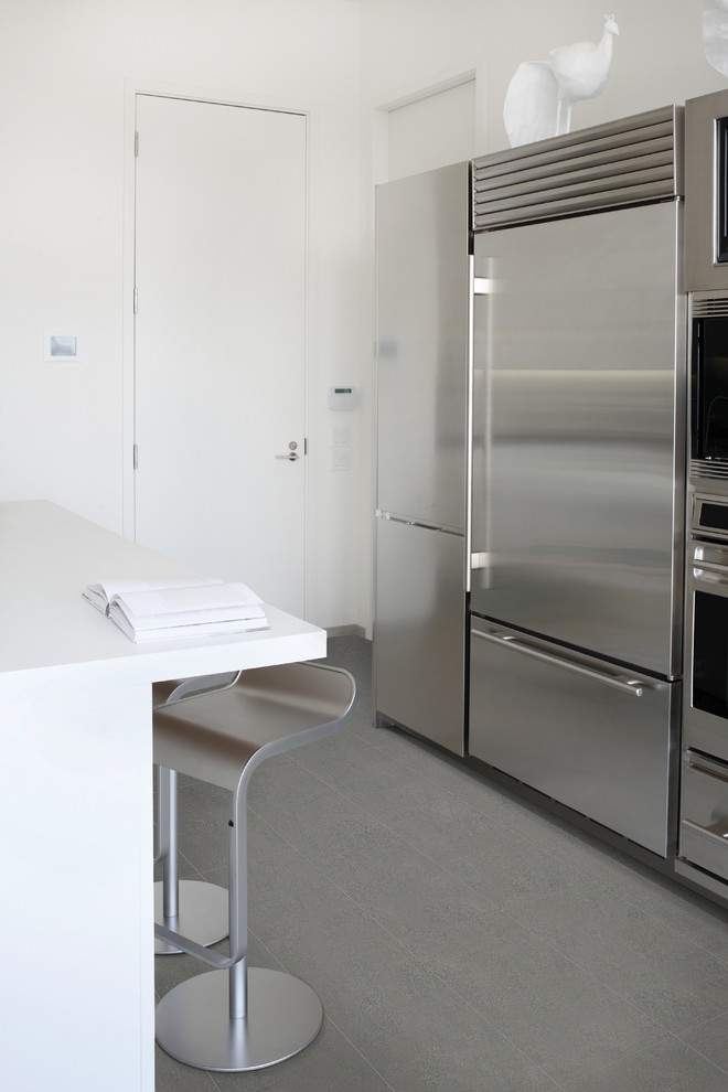 Example of a minimalist slate floor eat-in kitchen design in New York with flat-panel cabinets, white cabinets, stainless steel appliances and an island