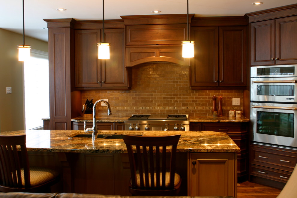 Пример оригинального дизайна: угловая кухня-гостиная в стиле неоклассика (современная классика) с врезной мойкой, фасадами с утопленной филенкой, темными деревянными фасадами, гранитной столешницей, бежевым фартуком, фартуком из каменной плитки и техникой под мебельный фасад