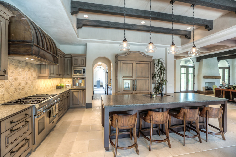 Inspiration for a large mediterranean l-shaped limestone floor and beige floor open concept kitchen remodel in Houston with an undermount sink, raised-panel cabinets, medium tone wood cabinets, granite countertops, beige backsplash, mosaic tile backsplash, paneled appliances and an island