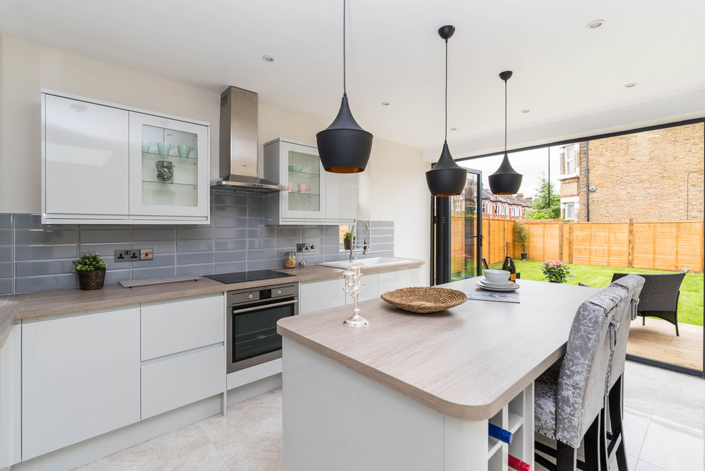 Photo of a large contemporary l-shaped open plan kitchen in London with a built-in sink, glass-front cabinets, grey cabinets, laminate countertops, grey splashback, metro tiled splashback, integrated appliances, ceramic flooring, an island and grey floors.