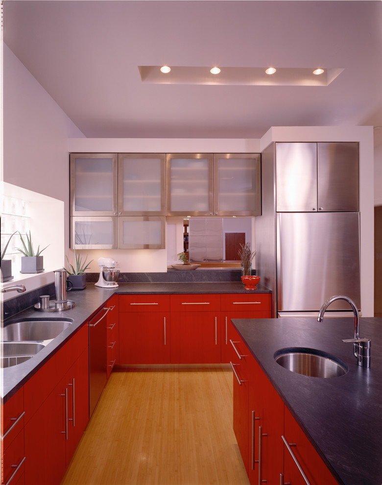 На фото: угловая кухня-гостиная среднего размера в современном стиле с красными фасадами, двойной мойкой, плоскими фасадами, техникой из нержавеющей стали, серым фартуком, полом из бамбука, островом и бежевым полом с