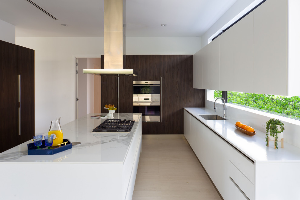 Design ideas for a large modern galley open plan kitchen in Miami with a built-in sink, dark wood cabinets, engineered stone countertops, white splashback, stainless steel appliances, limestone flooring, an island, beige floors and white worktops.