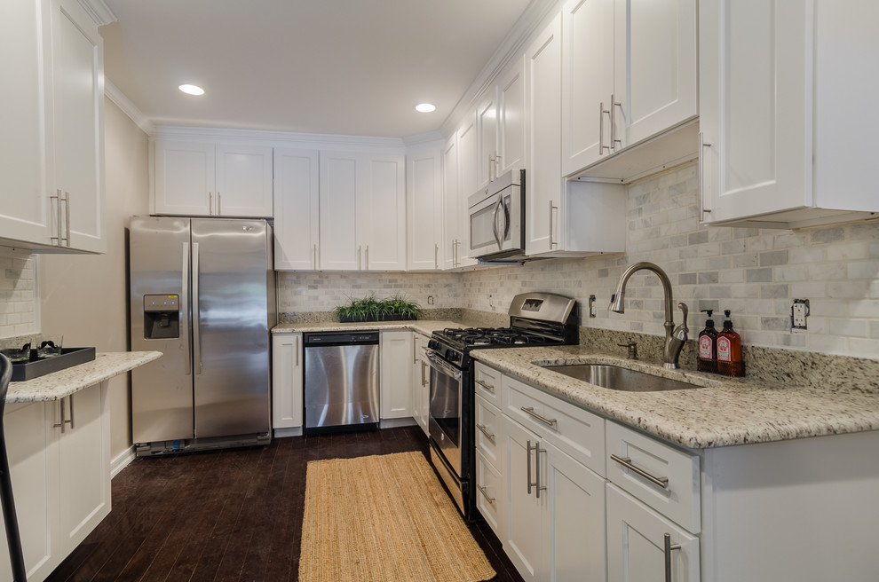 Inspiration for a mid-sized industrial u-shaped dark wood floor eat-in kitchen remodel in Baltimore with an undermount sink, shaker cabinets, white cabinets, granite countertops, white backsplash, marble backsplash, stainless steel appliances and no island
