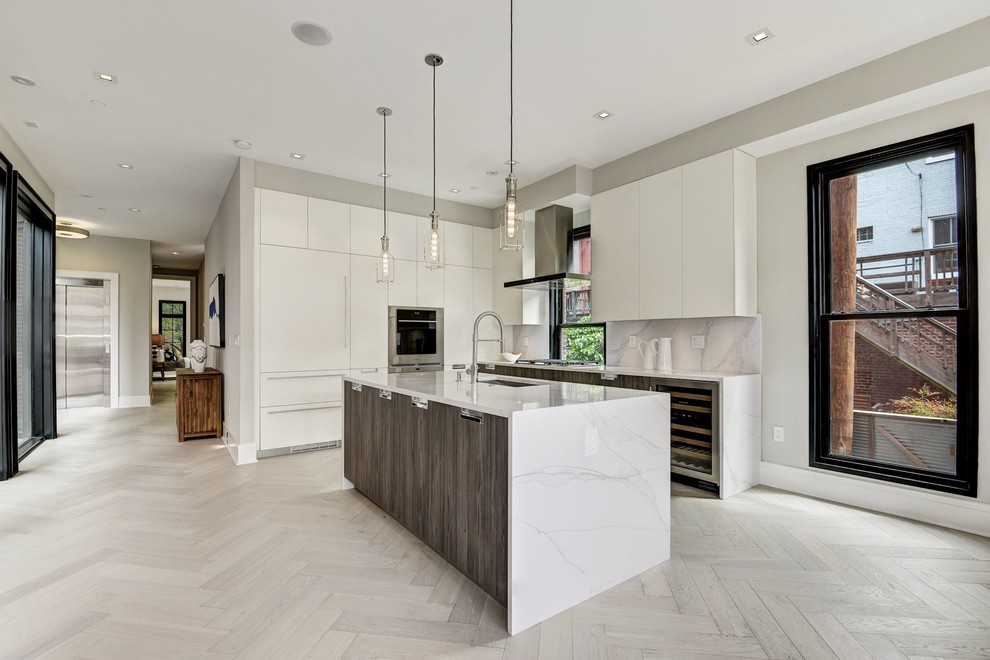 Modern inredning av ett kök, med en undermonterad diskho, släta luckor, vita skåp, bänkskiva i kvarts, vitt stänkskydd, rostfria vitvaror, ljust trägolv, en köksö och vitt golv