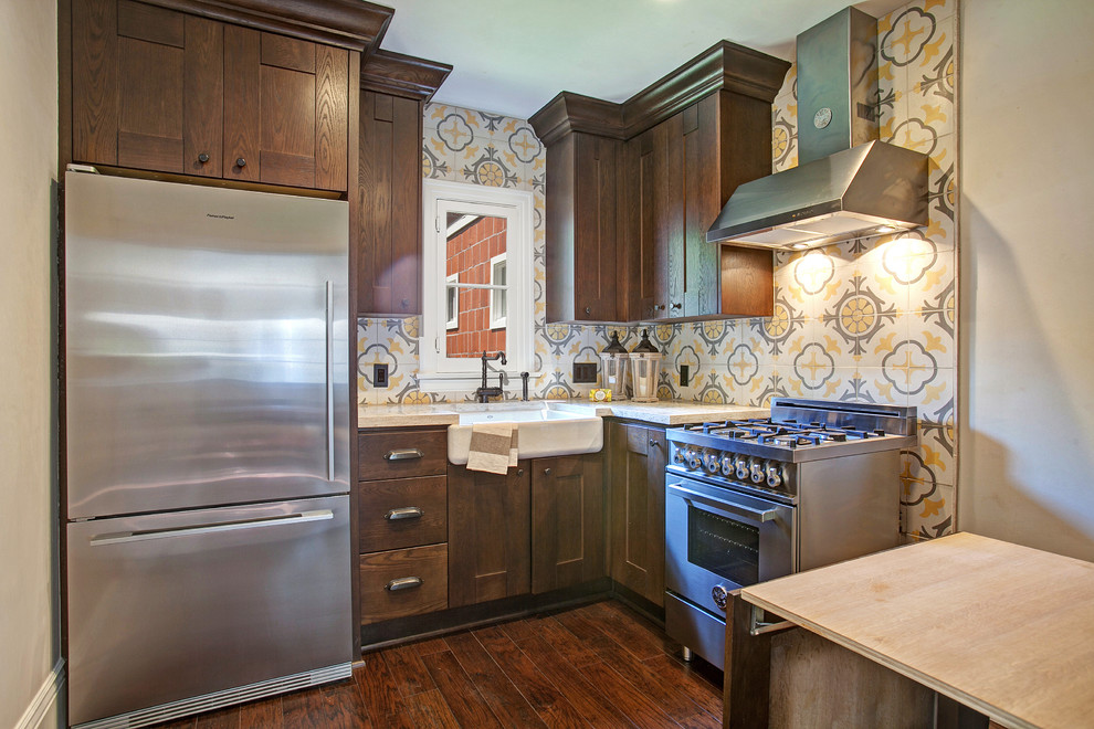 Klassisk inredning av ett l-kök, med en rustik diskho, luckor med infälld panel, skåp i mörkt trä och rostfria vitvaror