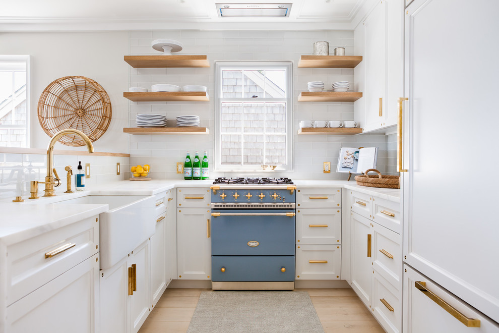 Example of a beach style u-shaped light wood floor kitchen design in Boston with a farmhouse sink, recessed-panel cabinets, white cabinets, white backsplash, subway tile backsplash, colored appliances and no island