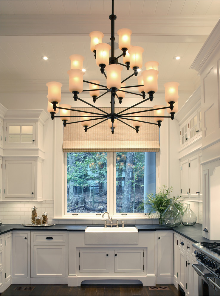 This is an example of a large rural u-shaped kitchen/diner in Atlanta with a belfast sink, shaker cabinets, white cabinets, white splashback, metro tiled splashback, stainless steel appliances, dark hardwood flooring and black floors.