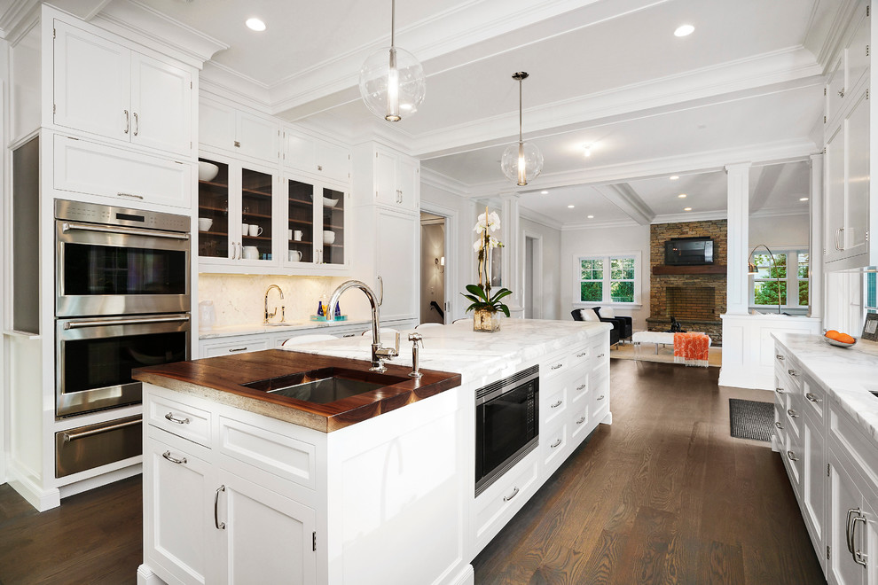 Example of a huge transitional u-shaped medium tone wood floor enclosed kitchen design in New York with a drop-in sink, beaded inset cabinets, white cabinets, marble countertops, paneled appliances and an island
