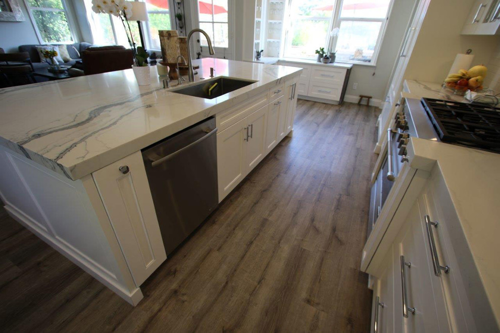 Example of a large urban l-shaped light wood floor and brown floor eat-in kitchen design in Orange County with a single-bowl sink, glass-front cabinets, white cabinets, marble countertops, gray backsplash, ceramic backsplash, stainless steel appliances, an island and white countertops