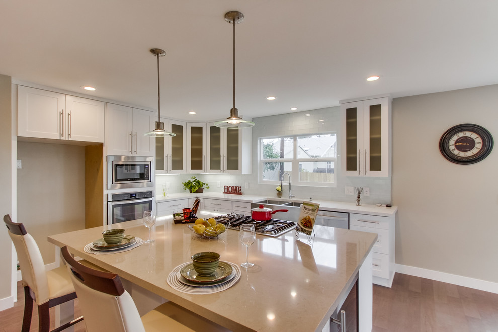 Moderne Küche mit Landhausspüle, Glasfronten, weißen Schränken, Küchenrückwand in Grau, Küchengeräten aus Edelstahl, hellem Holzboden und Kücheninsel in San Diego