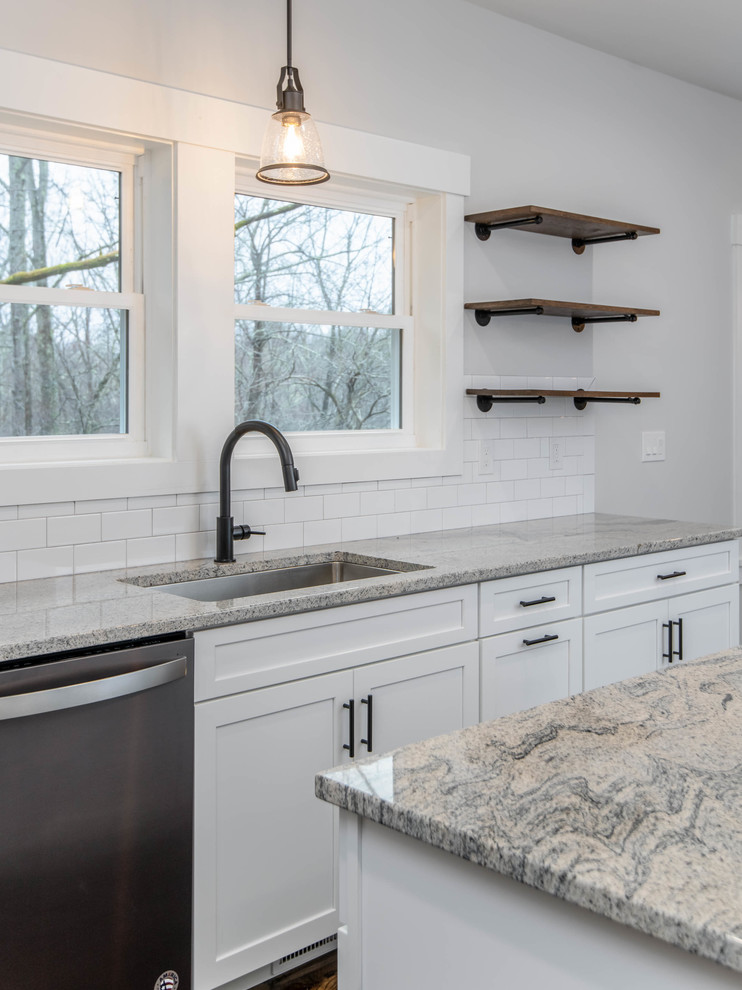 Foto på ett mellanstort funkis grå kök, med en undermonterad diskho, skåp i shakerstil, vita skåp, granitbänkskiva, vitt stänkskydd, stänkskydd i tunnelbanekakel, rostfria vitvaror, mörkt trägolv, en köksö och brunt golv