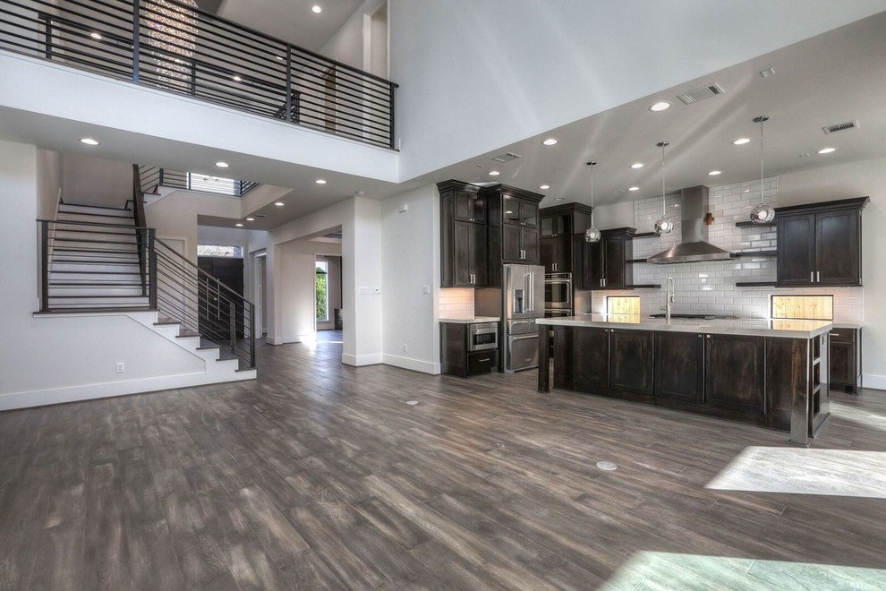 Inspiration for a large transitional l-shaped dark wood floor and brown floor open concept kitchen remodel in Houston with a farmhouse sink, shaker cabinets, dark wood cabinets, marble countertops, white backsplash, subway tile backsplash, stainless steel appliances and an island