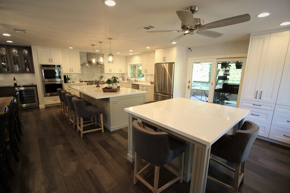 Inspiration for a large transitional l-shaped light wood floor and multicolored floor eat-in kitchen remodel in Orange County with a double-bowl sink, shaker cabinets, light wood cabinets, granite countertops, gray backsplash, ceramic backsplash, stainless steel appliances, two islands and white countertops