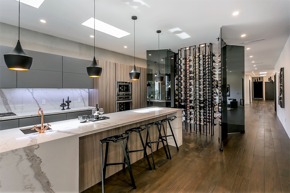 This is an example of a contemporary kitchen in Los Angeles with a submerged sink, flat-panel cabinets, grey cabinets, marble worktops, white splashback, marble splashback, stainless steel appliances, medium hardwood flooring, an island and brown floors.