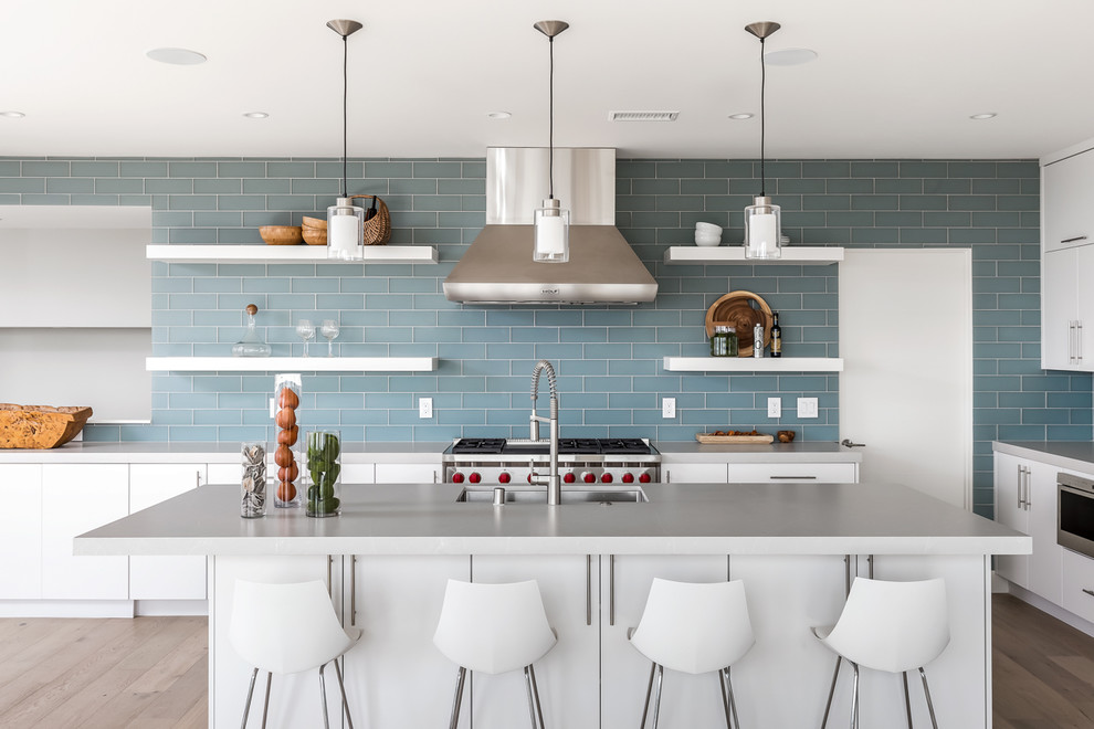 Inredning av ett modernt stort grå grått kök, med en undermonterad diskho, släta luckor, vita skåp, bänkskiva i kvarts, blått stänkskydd, stänkskydd i glaskakel, rostfria vitvaror, ljust trägolv, en köksö och beiget golv