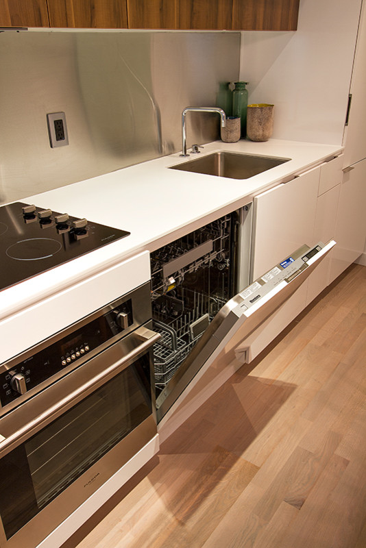 Idee per una piccola cucina moderna con lavello sottopiano, ante lisce, ante bianche, elettrodomestici in acciaio inossidabile, parquet chiaro e top bianco