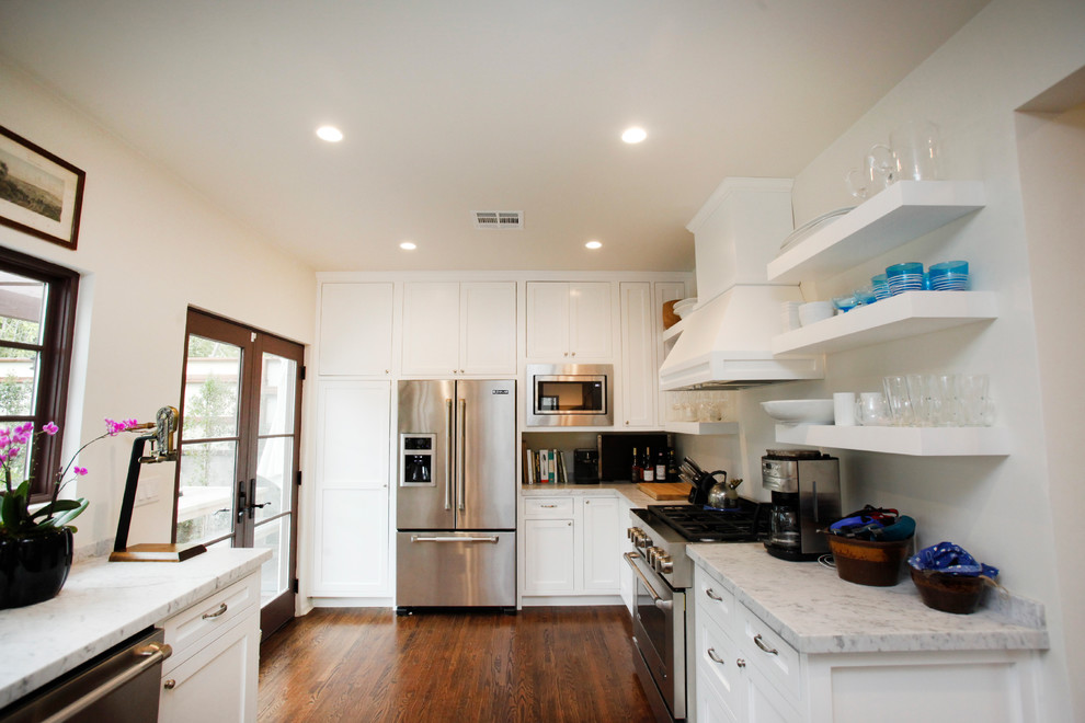 Inspiration for a mid-sized mediterranean u-shaped medium tone wood floor and brown floor enclosed kitchen remodel in Los Angeles with recessed-panel cabinets, white cabinets, marble countertops, stainless steel appliances and an island
