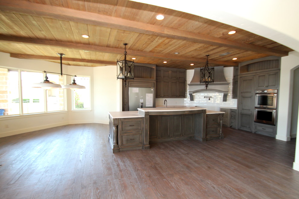 Example of a tuscan u-shaped light wood floor eat-in kitchen design in Dallas with an undermount sink, recessed-panel cabinets, gray cabinets, marble countertops, white backsplash, porcelain backsplash, stainless steel appliances and an island