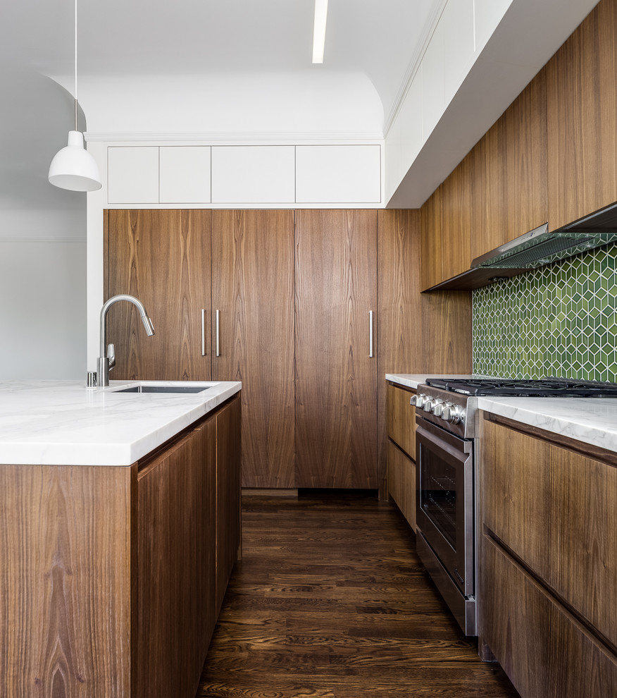 Modern inredning av ett kök, med en enkel diskho, släta luckor, skåp i mörkt trä, marmorbänkskiva, grönt stänkskydd, stänkskydd i keramik, rostfria vitvaror, mörkt trägolv och en köksö