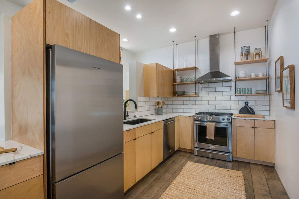 Photo of a medium sized modern l-shaped open plan kitchen in Albuquerque with a submerged sink, flat-panel cabinets, light wood cabinets, marble worktops, white splashback, metro tiled splashback, stainless steel appliances, medium hardwood flooring, a breakfast bar, brown floors and white worktops.