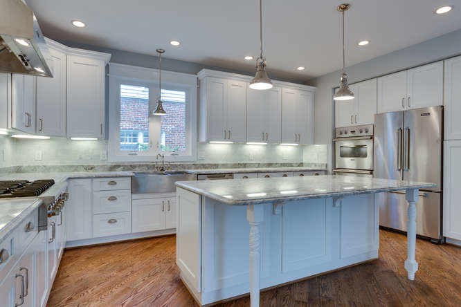 This is an example of a medium sized classic l-shaped enclosed kitchen in DC Metro with a belfast sink, recessed-panel cabinets, white cabinets, granite worktops, grey splashback, stone tiled splashback, stainless steel appliances, medium hardwood flooring, an island and brown floors.