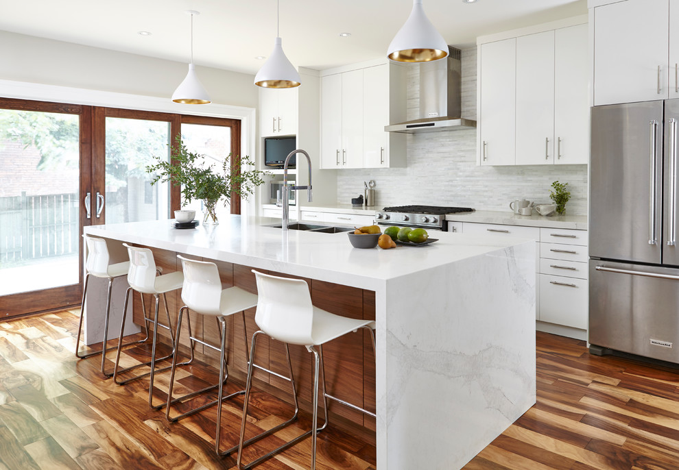 Inspiration for a transitional galley medium tone wood floor and brown floor kitchen remodel in Toronto with a double-bowl sink, flat-panel cabinets, white cabinets, white backsplash, matchstick tile backsplash, stainless steel appliances and an island
