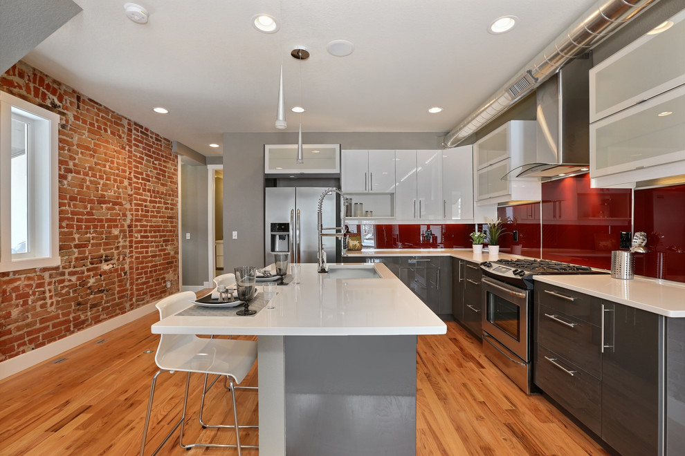 Modern inredning av ett kök, med en nedsänkt diskho, luckor med glaspanel, vita skåp, laminatbänkskiva, rött stänkskydd, glaspanel som stänkskydd, rostfria vitvaror, ljust trägolv och en köksö
