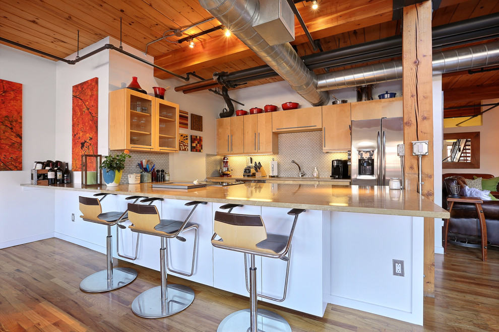 Foto på ett industriellt kök, med en undermonterad diskho, släta luckor, skåp i mellenmörkt trä, vitt stänkskydd, stänkskydd i mosaik, rostfria vitvaror, mellanmörkt trägolv och en halv köksö