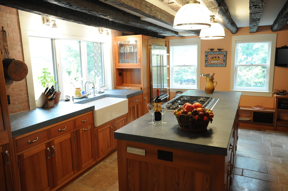 Lantlig inredning av ett kök, med en rustik diskho, skåp i shakerstil, skåp i mellenmörkt trä, bänkskiva i täljsten, rostfria vitvaror, kalkstensgolv och en köksö