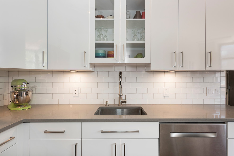 This is an example of a small contemporary l-shaped enclosed kitchen in New York with a submerged sink, white cabinets, white splashback, metro tiled splashback, stainless steel appliances, ceramic flooring, no island and glass-front cabinets.