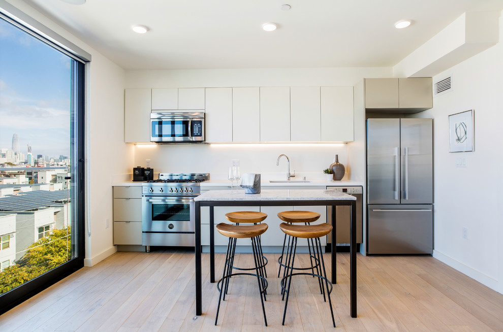 サンフランシスコにあるコンテンポラリースタイルのおしゃれなI型キッチン (アンダーカウンターシンク、フラットパネル扉のキャビネット、ベージュのキャビネット、白いキッチンパネル、シルバーの調理設備、淡色無垢フローリング、アイランドなし、ベージュの床) の写真