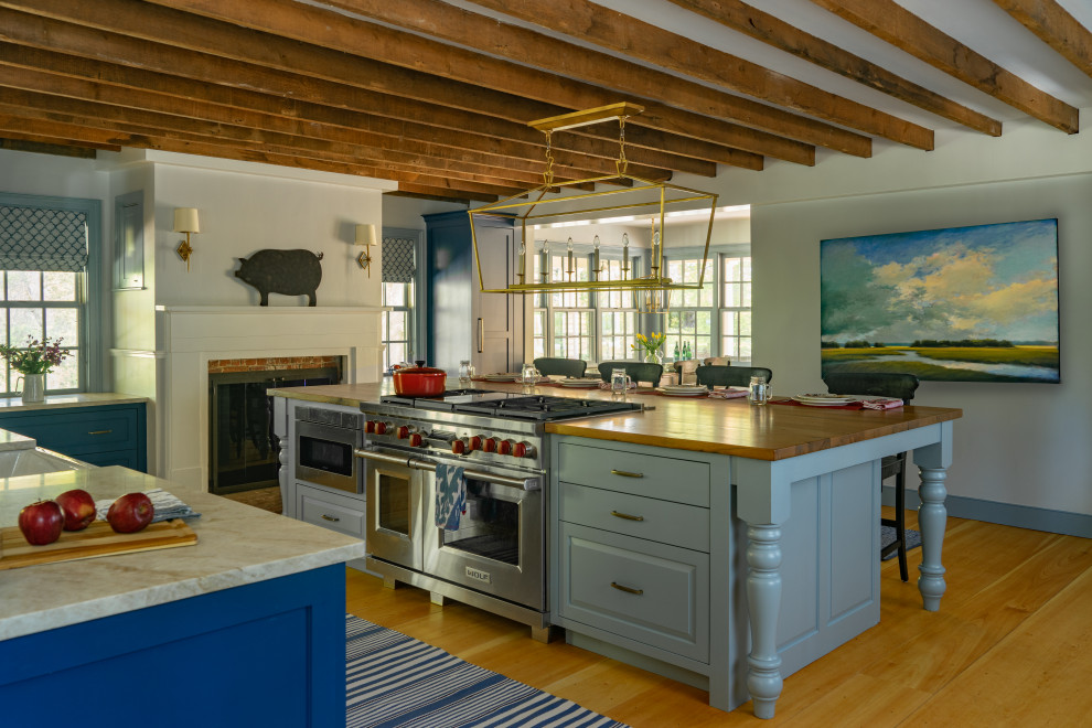 Example of a farmhouse l-shaped medium tone wood floor and brown floor kitchen design in Boston with a farmhouse sink, recessed-panel cabinets, blue cabinets, wood countertops, stainless steel appliances, an island and brown countertops
