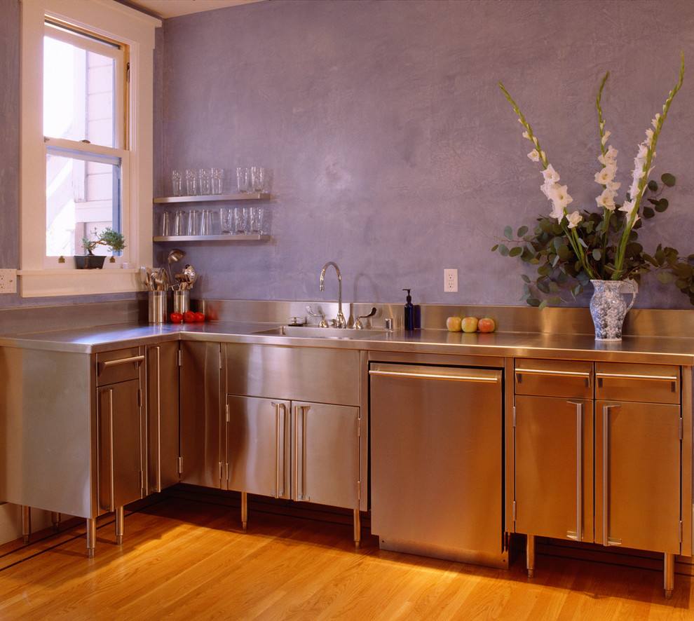 Exempel på ett l-kök, med en integrerad diskho, skåp i rostfritt stål, bänkskiva i rostfritt stål, rostfria vitvaror och mellanmörkt trägolv