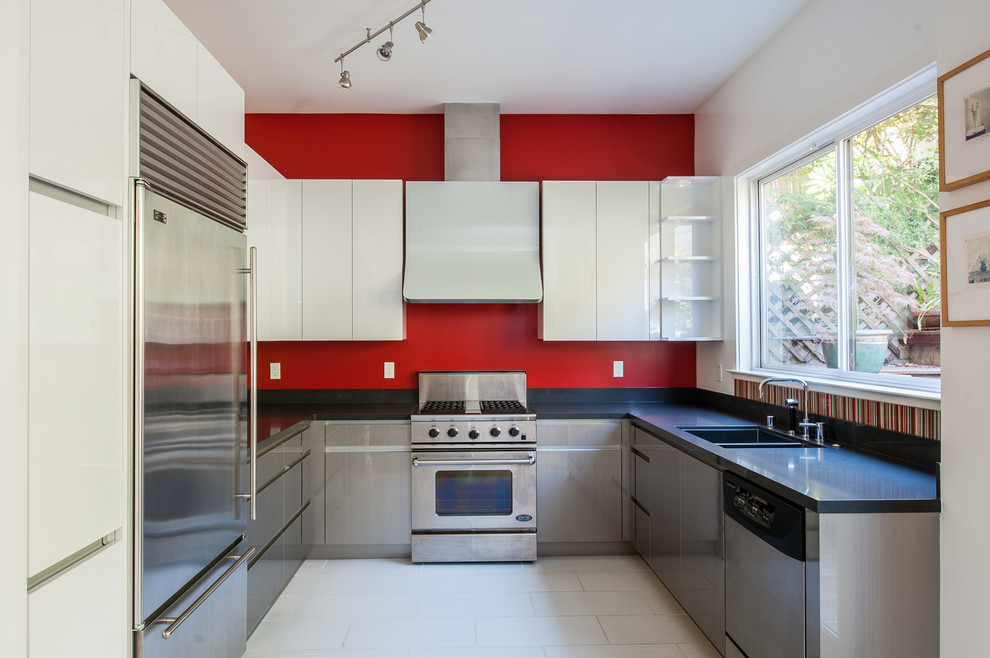 Réalisation d'une cuisine design en U avec un évier encastré, un placard à porte plane, des portes de placard grises, une crédence rouge et un électroménager en acier inoxydable.
