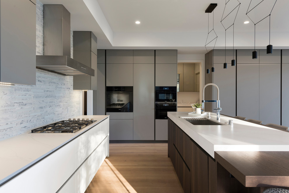 Inspiration for a large contemporary u-shaped kitchen/diner in Minneapolis with a submerged sink, grey cabinets, medium hardwood flooring, an island, brown floors, white worktops, flat-panel cabinets, grey splashback and black appliances.