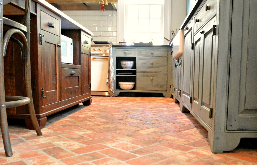 Bild på ett avskilt, stort lantligt grå grått u-kök, med en rustik diskho, luckor med upphöjd panel, blå skåp, marmorbänkskiva, vitt stänkskydd, stänkskydd i tunnelbanekakel, integrerade vitvaror, tegelgolv, en köksö och rött golv