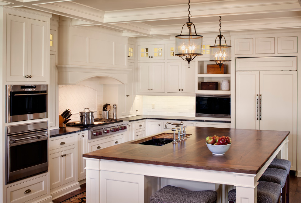 Example of a farmhouse kitchen design in Milwaukee with an undermount sink, beaded inset cabinets, white cabinets, wood countertops, white backsplash, subway tile backsplash and paneled appliances