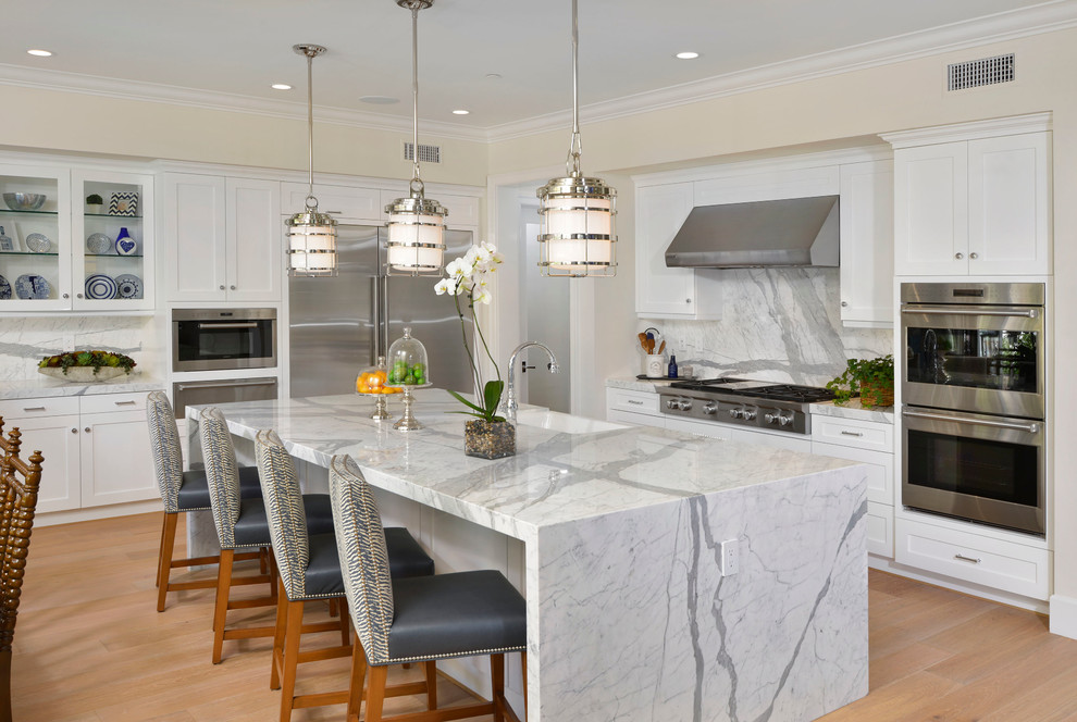 Design ideas for a classic grey and white kitchen in Orange County with a belfast sink, shaker cabinets, white cabinets, white splashback, stainless steel appliances, light hardwood flooring and an island.