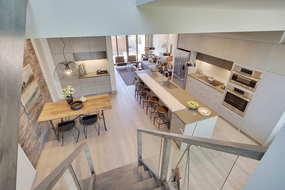 Eat-in kitchen - contemporary l-shaped medium tone wood floor eat-in kitchen idea in Calgary with a single-bowl sink, flat-panel cabinets, gray cabinets, quartzite countertops, white backsplash, ceramic backsplash, stainless steel appliances and an island