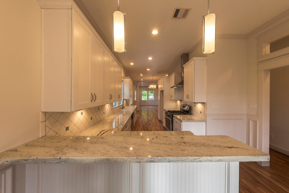 Example of a mid-sized arts and crafts galley light wood floor open concept kitchen design in Houston with a drop-in sink, shaker cabinets, white cabinets, granite countertops, white backsplash, ceramic backsplash, stainless steel appliances and a peninsula