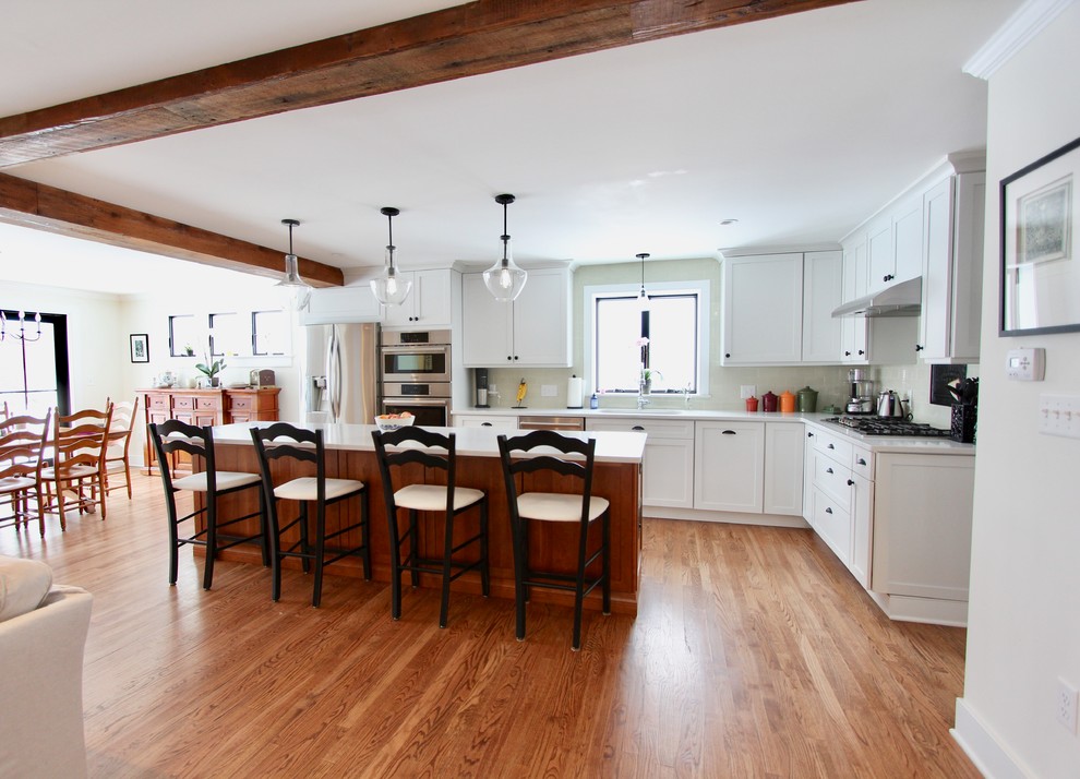 Inredning av ett lantligt mycket stort vit vitt kök, med en undermonterad diskho, skåp i shakerstil, vita skåp, bänkskiva i kvarts, beige stänkskydd, stänkskydd i keramik, rostfria vitvaror, mellanmörkt trägolv, en köksö och brunt golv