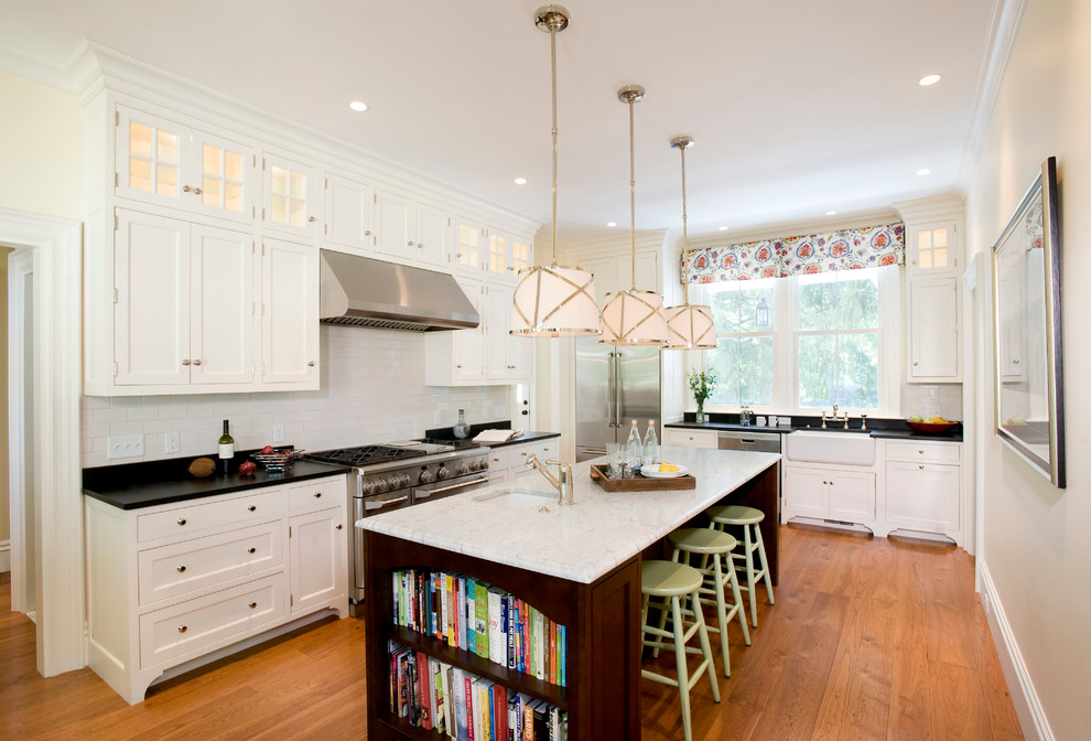 Large elegant l-shaped medium tone wood floor kitchen photo in Boston with a farmhouse sink, beaded inset cabinets, white cabinets, white backsplash, stainless steel appliances, subway tile backsplash, granite countertops and an island