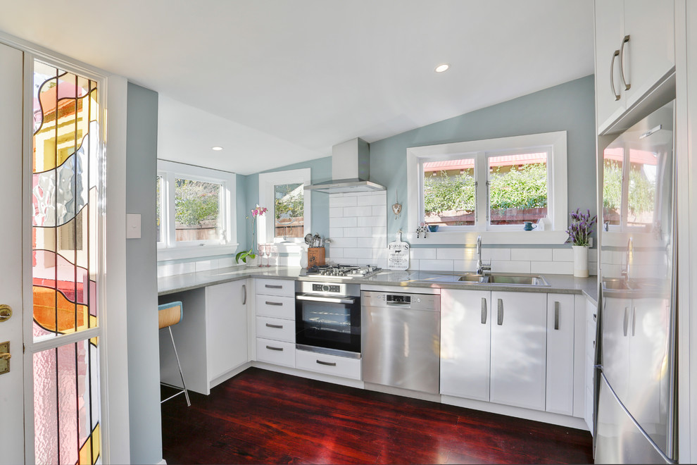 This is an example of a small classic u-shaped kitchen in Christchurch with a double-bowl sink, raised-panel cabinets, grey cabinets, engineered stone countertops, white splashback, ceramic splashback, stainless steel appliances, painted wood flooring, no island, red floors and grey worktops.