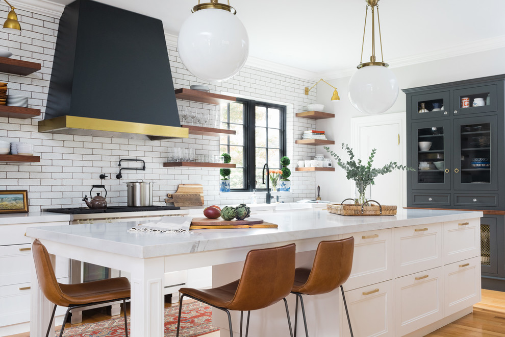 Klassische Küche mit Landhausspüle, Schrankfronten mit vertiefter Füllung, weißen Schränken, Küchenrückwand in Weiß, Rückwand aus Metrofliesen, braunem Holzboden, Kücheninsel und braunem Boden in Boston