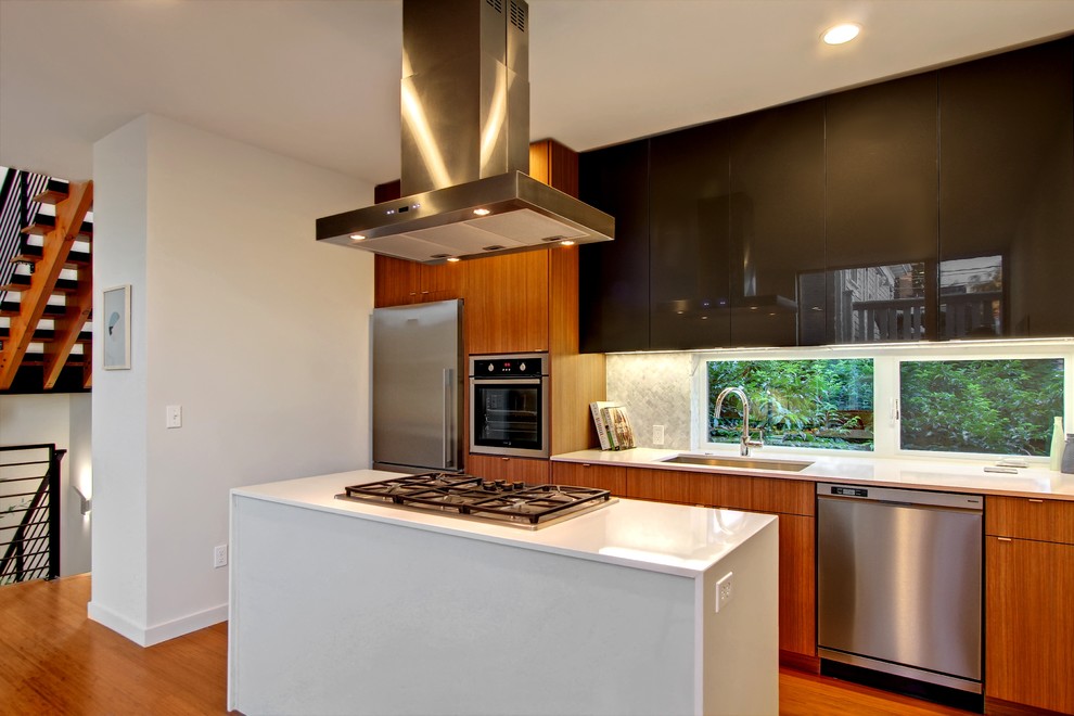 Modelo de cocina actual con fregadero bajoencimera, armarios con paneles lisos, puertas de armario negras, salpicadero blanco, electrodomésticos de acero inoxidable y salpicadero de azulejos de piedra