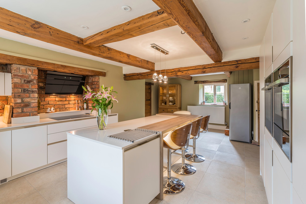 Photo of a farmhouse galley kitchen in Cheshire with flat-panel cabinets, white cabinets, wood worktops, red splashback, brick splashback, stainless steel appliances, an island and beige floors.