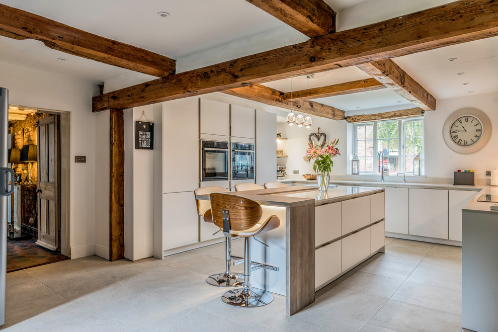 This is an example of a country kitchen in Cheshire with flat-panel cabinets, white cabinets and a breakfast bar.